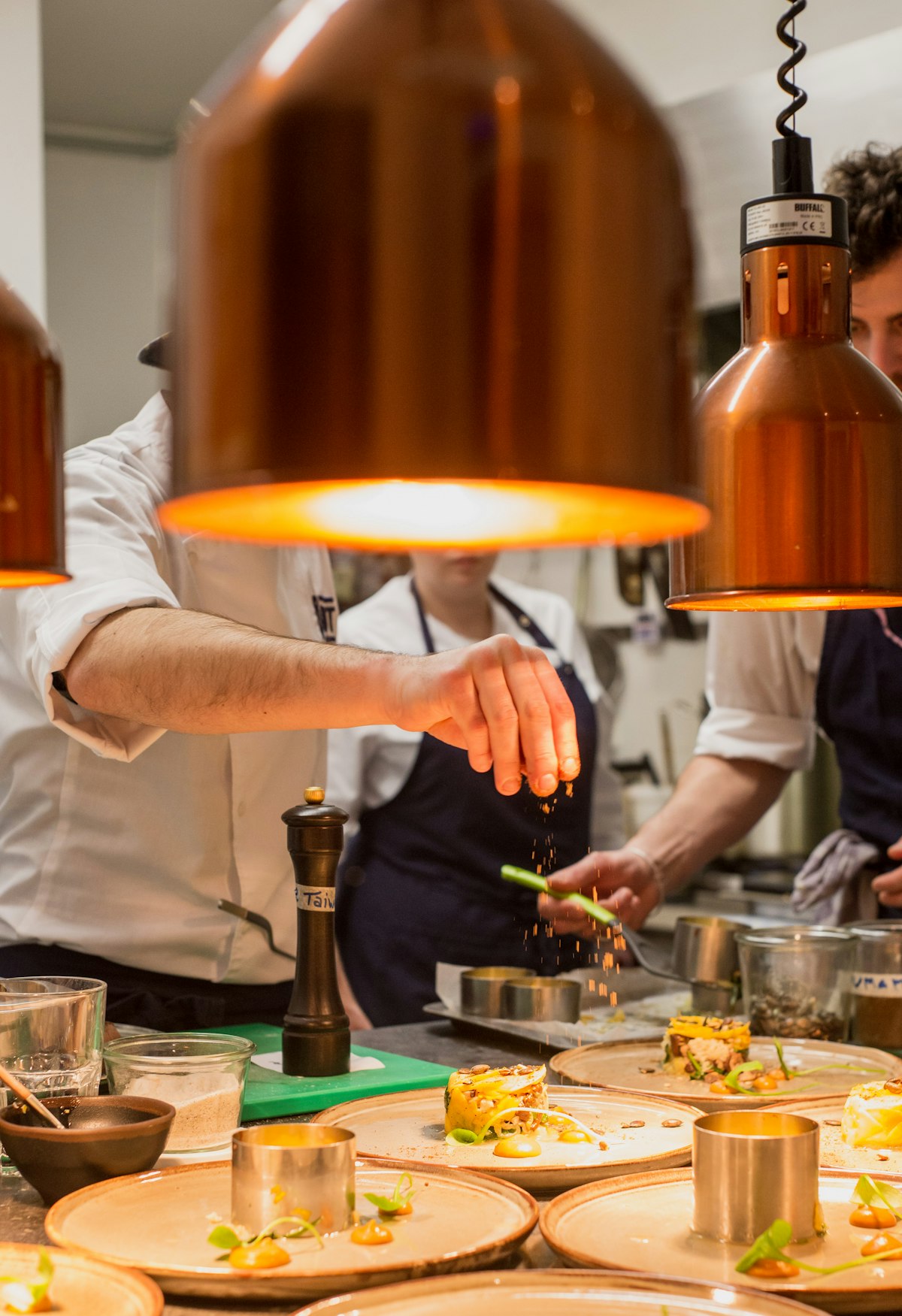 Chef's hand seasoning plated dishes under heat lamps
