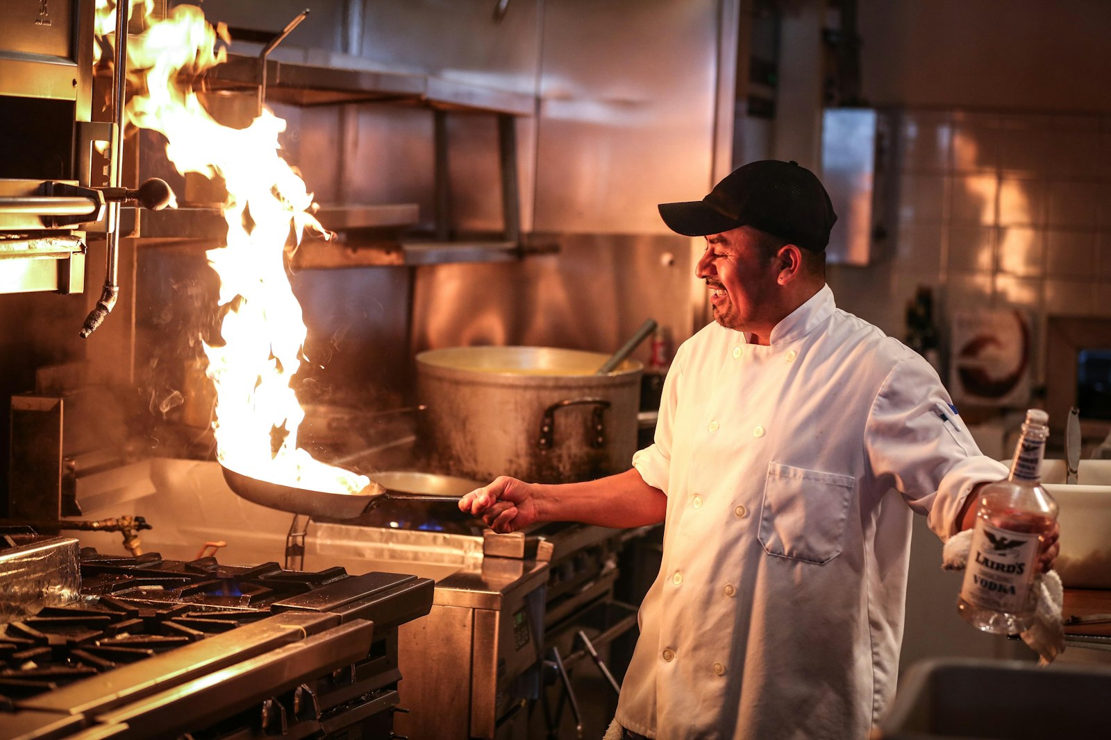 Chef flambéing a pan with huge flames in a dark kitchen